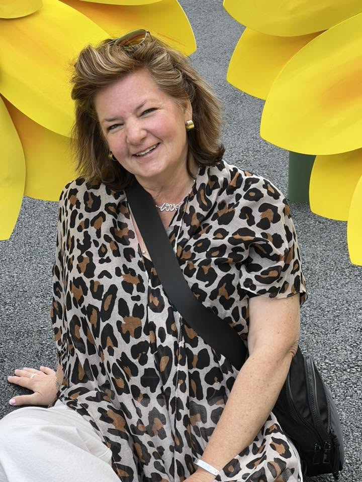 Monica Shupe, Thread the Needle Stitchery’s store manager and official Yarn Yoda, smiling among yellow flowers.
