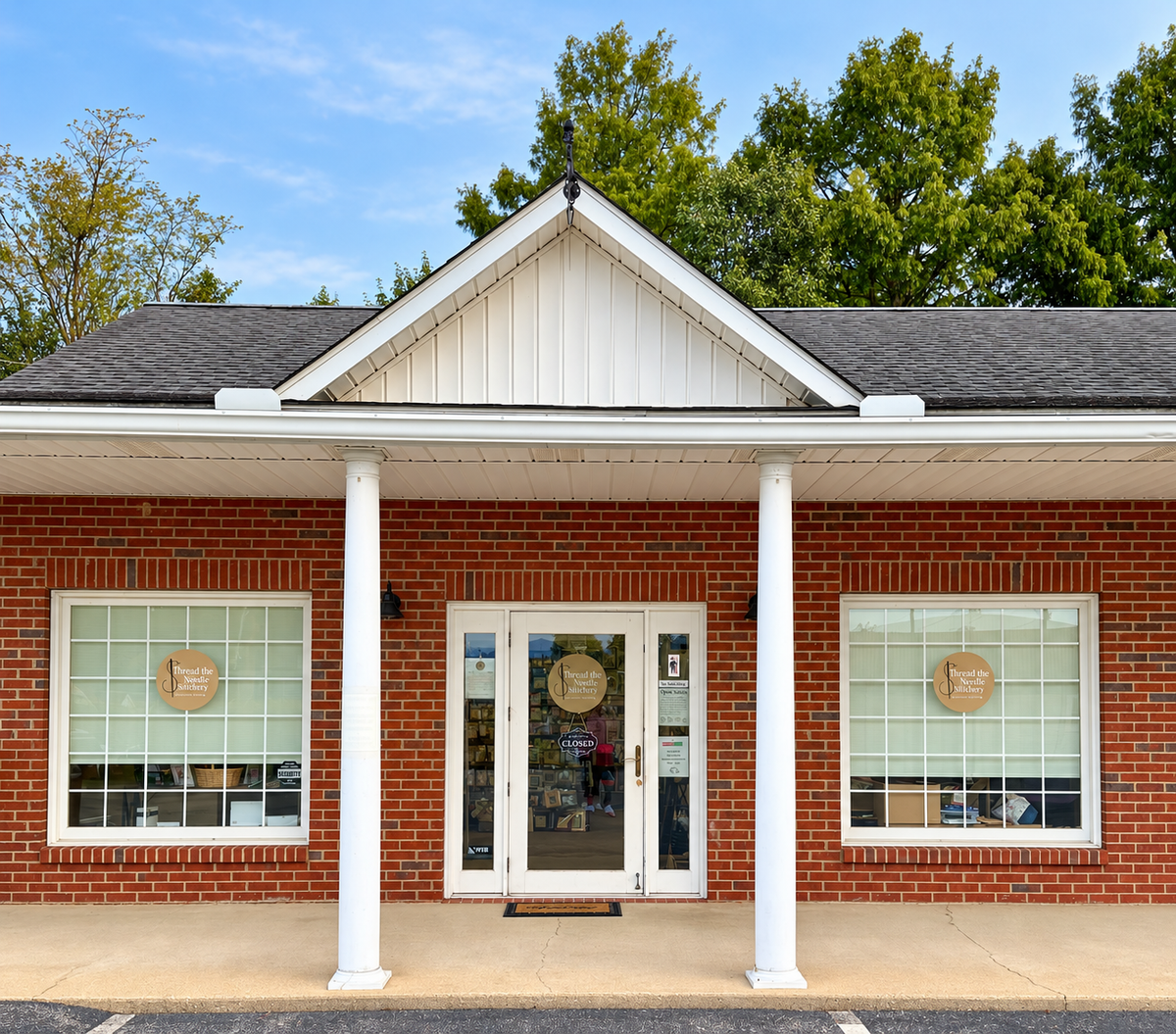 Thread the Needle Stitchery storefront in Greeneville, Tennessee, with a brick facade, white columns, and shop signs in the windows.